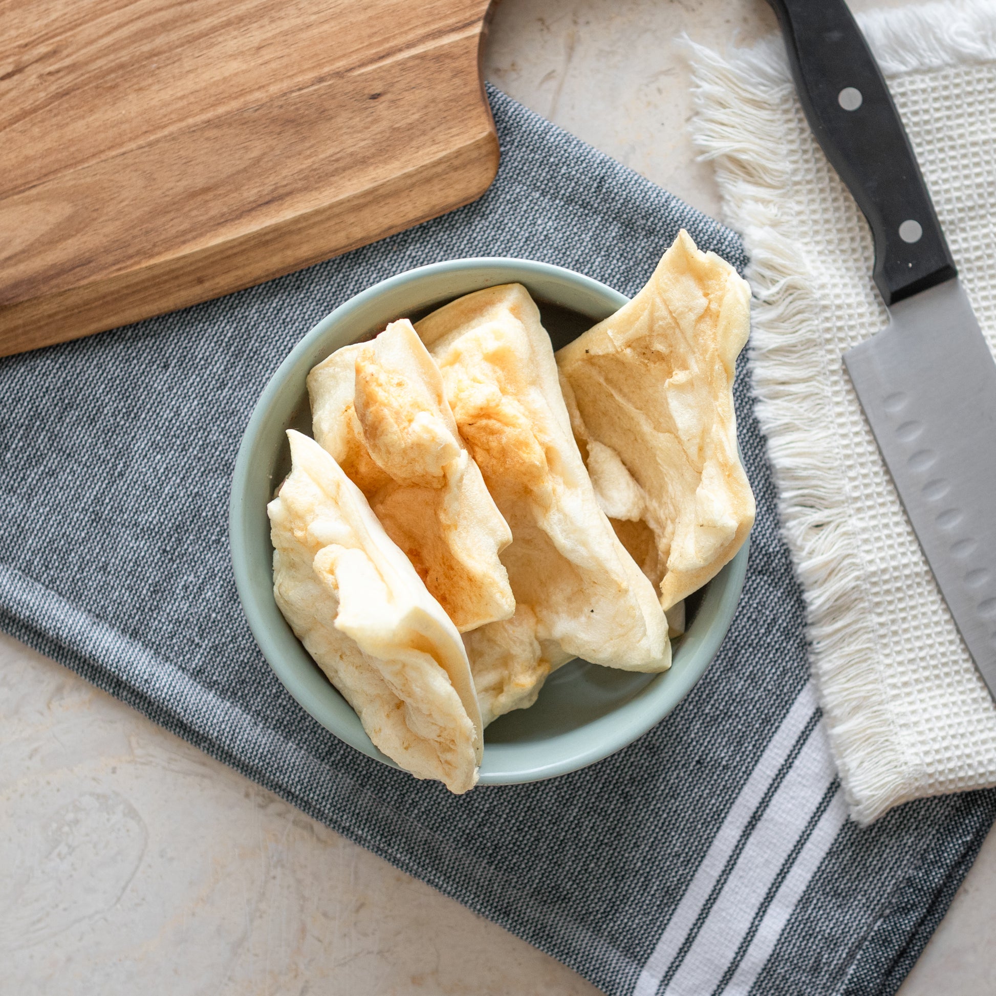 Bowl of All-Natural Beef Cheek Chips, a high-protein, long-lasting rawhide alternative for dogs, showcased on a textured fabric background.